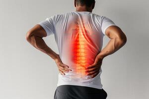 Man in a white shirt holding lower back in pain, illustrating back pain and spine health related to physiotherapy and injury management.