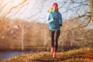 Woman jogging in winter attire on a path, emphasizing the importance of staying active and warm during colder months to prevent injuries.
